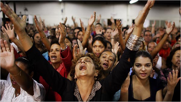 A woman with an audience behind her hands up praising God