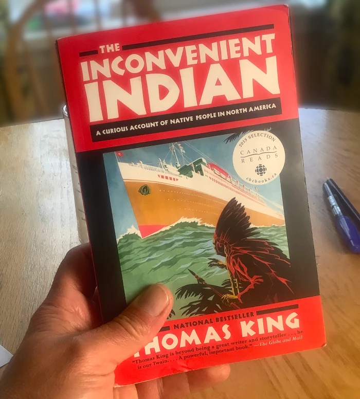 A hand holding Thomas King's book, The Inconvenient Indian